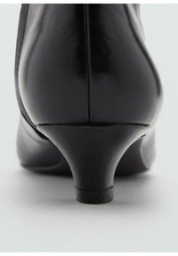 Černá kožená dámská bota na podpatku s hladkým lesklým povrchem, zakřiveným podpatkem a minimalistickým designem. Podpatek se zužuje k zaoblenému základu.