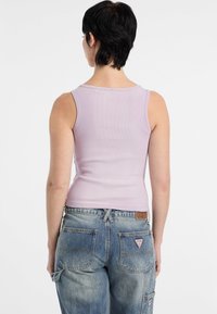 Top a canotta a coste viola chiaro con un design aderente, abbinata a jeans in denim blu larghi con due tasche posteriori e una patch con il logo.