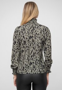 Olivengrøn bluse med sort dyreprint, med høj flæset krave og smockede manchetter, lavet af et letvægtsstof.