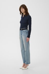 Polo de manga larga azul marino con tapeta de botones, combinado con vaqueros de pierna recta en azul claro y tacones blancos de punta fina. Diseño simple y minimalista.