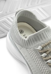 Graue gestrickte Sneaker mit einem schlichtem Design, strukturiertem Stoff und funkelnden Akzenten an der Schnürung. Weiße Gummisohle mit strukturiertem Profil.