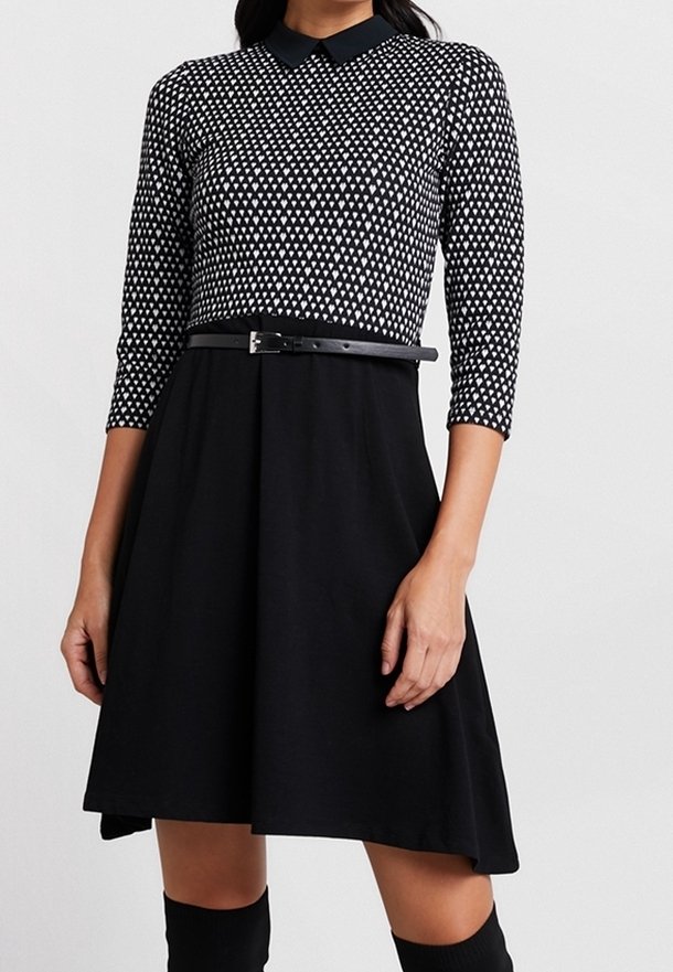 Robe noire avec un haut ajusté arborant un motif en losange blanc, un col, des manches trois-quarts et une ceinture noire à la taille.
