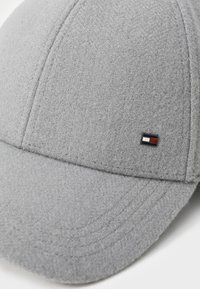 Grå uld baseball cap med en tekstureret overflade, der har et lille sort, hvidt og rødt logo-tag på siden samt broderede detaljer.