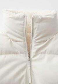 Witte pufferjack met een hoge kraag, met een zichtbare rits en een zachte, gevoerde fleece binnenkant. Glad buitenmateriaal met gestikte secties.