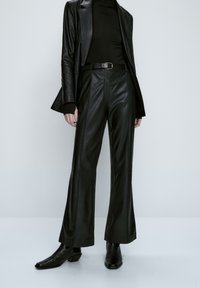 Zwarte leren flared broek met een hoge taille en zichtbare stikdetails. Gecombineerd met een bijpassende zwarte leren blazer en een nauwsluitende turtleneck.