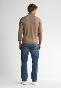 Pull en maille marron clair avec un col montant, associé à un jean en denim bleu décontracté et des baskets blanches. Texture lisse, design décontracté.