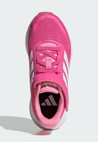 Basket de sport rose avec une tige en maille, fermeture à lacets et Velcro, trois rayures blanches et une semelle texturée. L'intérieur présente des détails de logo.