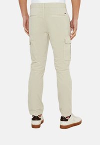 Pantalones cargo beige con bolsillos laterales, corte ajustado, fabricados en material de algodón. Presenta una etiqueta de logo en la cintura trasera.