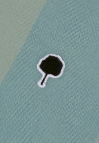 Hellgrüner, strukturierter Stoff mit einem schwarzen, gestickten Baumdesign, das in Weiß umrandet ist und sich auf einem kontrastierenden grünen Bereich befindet.