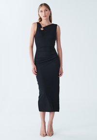 Schulterfreies schwarzes Midi-Kleid mit Knoten-Detail an der Vorderseite, strukturiertem Stoff und figurnahem Schnitt. Modell trägt nudefarbene Sandalen.