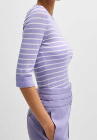 Ljuslila, randig stickad topp med trekvartslånga ärmar och rundad halsringning, i kombination med högmidjade lavendelfärgade byxor.