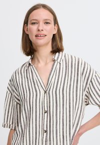Camicia in lino con bottoni e maniche corte, caratterizzata da righe verticali bianche e nere e colletto a punta.