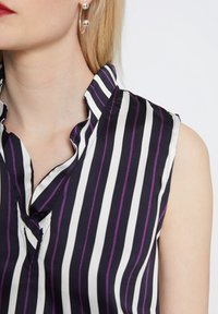 Blusa senza maniche in righe verticali blu navy, bianche e viola; il tessuto sembra setoso con un colletto pieghettato e un dettaglio a scollo a V.