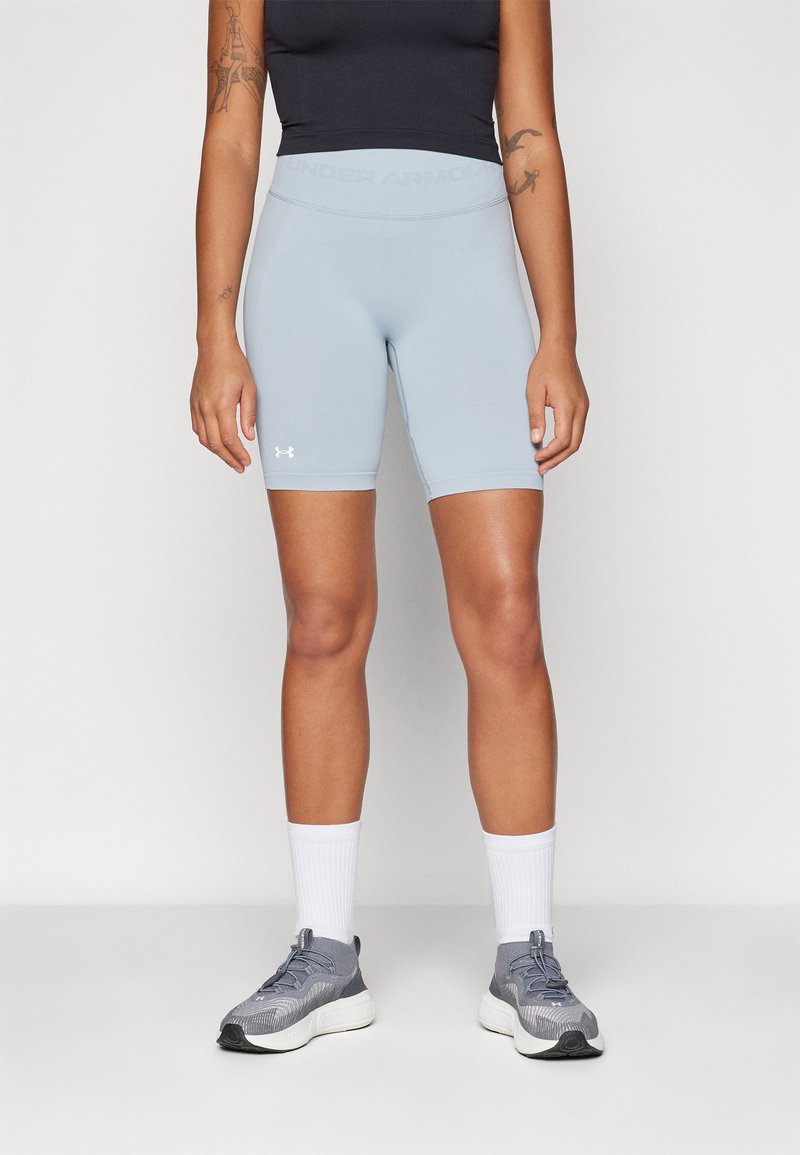 Világoskék sportnadrág sima textúrával és rugalmas derékpánttal, amelyen az "Under Armour" márkajelzés található. Szürke sportcipővel és fehér zoknival párosítva.