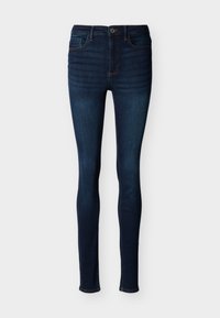 Σκούρα μπλε στενά τζιν με κουμπί και φερμουάρ μπροστά, σχεδιασμό με πέντε τσέπες και ορατές ραφές σε απλό λευκό φόντο.