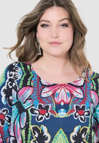 Top con estampado floral hecho de tejido liviano, con colores vibrantes como azul, rosa y verde. Cuello redondeado, con detalles en toda la prenda.