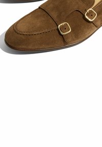 Bruine suède loafers met een gladde afwerking, ronde neus, dubbele gesp-accenten en een dunne, slanke zool.