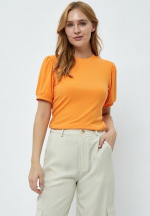 Camiseta de algodón naranja con textura de canalé y mangas cortas abullonadas, combinada con pantalones beiges claros de corte relajado y escote redondo.