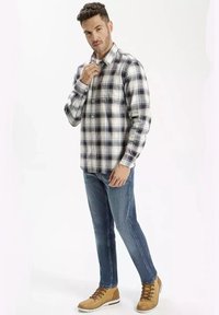 Koszula w kratę z guzikami w kolorze granatowym, białym i szarym, zestawiona z niebieskimi dżinsami i brązowymi wiązanymi butami. Koszula ma długie rękawy i kołnierz.