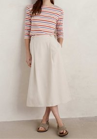 Randig långärmad topp i rosa, orange och lavendel, ihop med en beige, flödande midiklänning med sidofickor och knappdetaljer, bärs med grå sandaler.