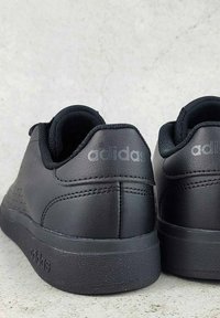 Čierne kožené tenisky s hladkým povrchom, perforovanými detailmi, polstrovaným golierom a embosovaným logom na päte a na boku.