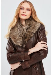 Brown leather coat featuring a large, soft faux fur collar. The coat has zippered pockets and button accents, with a tailored fit.