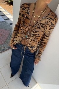 Tiger print, brown and black open-front blouse with long sleeves, paired with wide-leg dark denim jeans and layered gold necklaces.