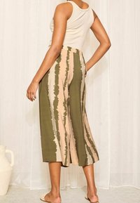 Kalhoty culotte se pruhovaným vzorem v olivově zelené a béžové barvě, vyrobené z texturované tkaniny. Pas je elastický pro pohodlí.