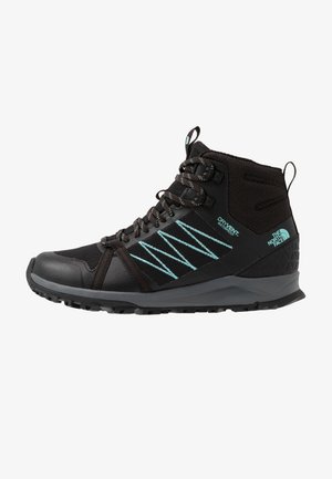 Bota de senderismo negra de altura media con costuras en zigzag turquesa, etiqueta impermeable, tobillo acolchado y suela resistente de The North Face.