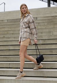 Rutet flannel skjorte i beige og brun, beige mini nederdel, sort håndtaske og beige sneakers med struktureret detaljering, går ned ad betontrapper.
