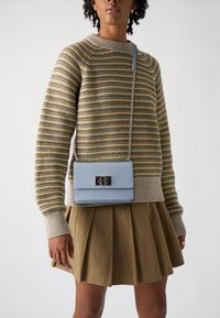 Maglione a righe in beige e grigio, abbinato a una borsa a tracolla azzurro chiaro con una chiusura nera, indossato con una gonna pieghettata marrone.