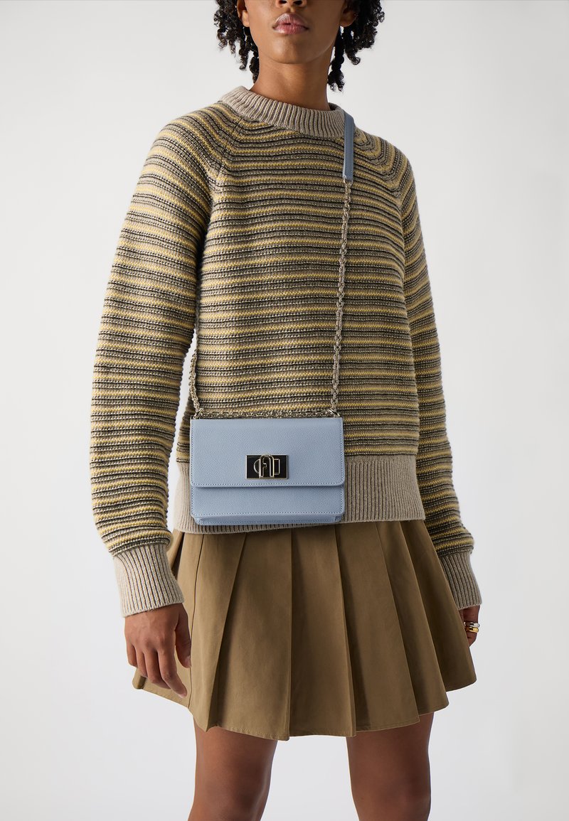 Maglione a righe in beige e grigio, abbinato a una borsa a tracolla azzurro chiaro con una chiusura nera, indossato con una gonna pieghettata marrone.