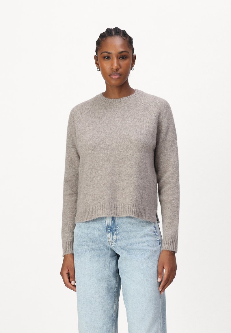Lichtgrijze gebreide trui met een ribbelboord aan de ronde hals, lange mouwen en zijsplitten, gecombineerd met lichtblauwe jeans. Zachte textuur.