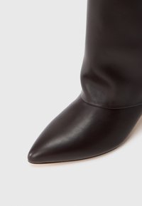 Botín negro de cuero hasta el tobillo con punta afilada y textura lisa, que presenta un ajuste ceñido alrededor del tobillo y un diseño minimalista.