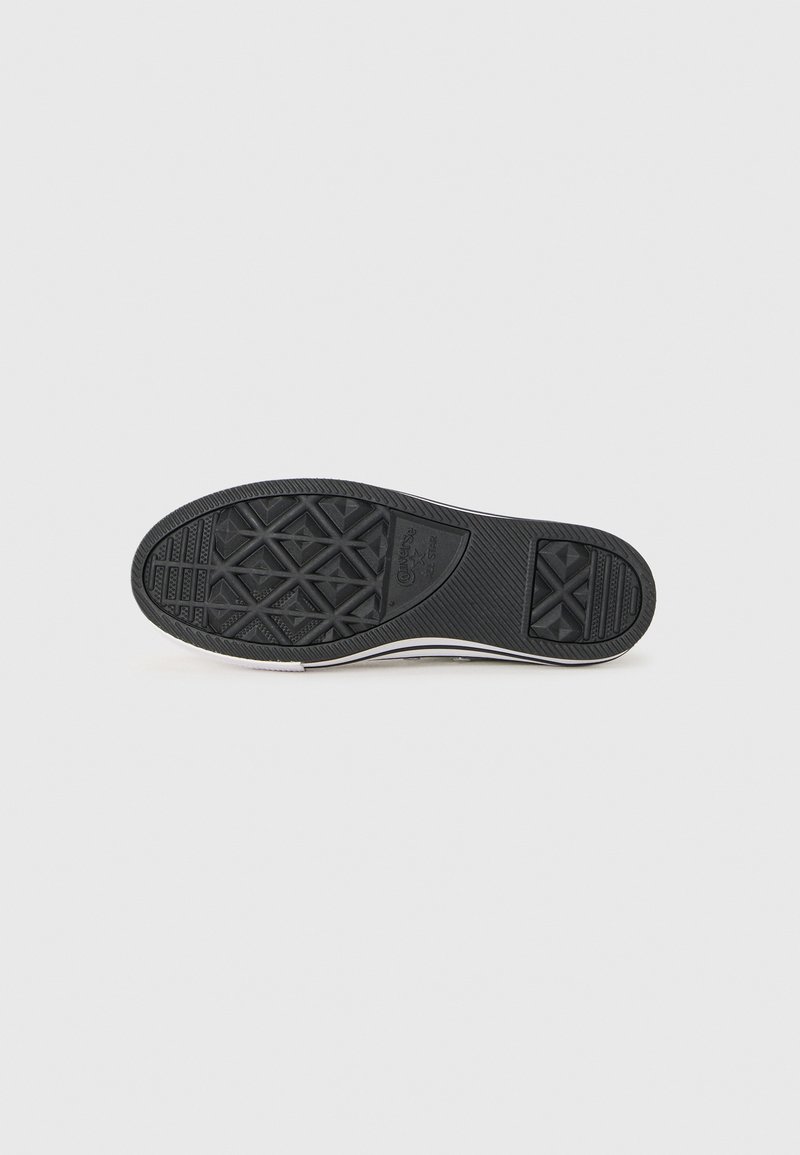 Suela de zapato de goma negra con patrones de agarre texturizados, con un borde redondeado y franjas laterales blancas. No se ven otros detalles.