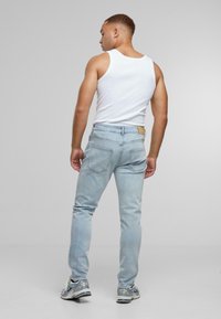 Világoskék, slim fit farmernadrág, hátul barna bőrpöttyel és egyszerű varrással. Fehér top és sportcipő társaságában viselve.