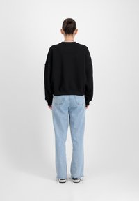 Felpa nera oversize con spalle abbassate e orlo a coste, abbinata a jeans dritti azzurri e sneakers in bianco e nero.