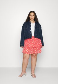 Casaco de ganga cropped, t-shirt branca, saia rodada de flores vermelhas em camadas e sandálias de salto bege. Apresenta camadas com ondulações e detalhes em estampado floral.