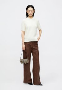 Pull crème à manches courtes, pantalon marron à jambes larges et petit sac à main texturé gris avec deux poignées et des accents bouclés.