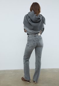 Sivkasta pleteno pulover, položen preko ramen, v kombinaciji z sivimi kavbojkami z visokim pasom, ki imajo zbledel videz in vidne zadnje žepe.