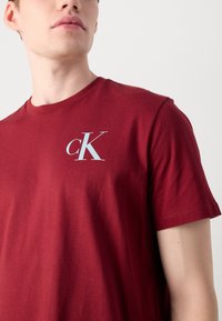 Burgundi színű pamut póló, világoskék "cK" logóval a mellrészén. Klasszikus kerek nyakú, rövid ujjú dizájn, puha tapintással.