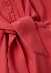 Tissu rouge noué avec trois boutons recouverts de tissu visibles en arrière-plan, montrant clairement la texture et les plis.