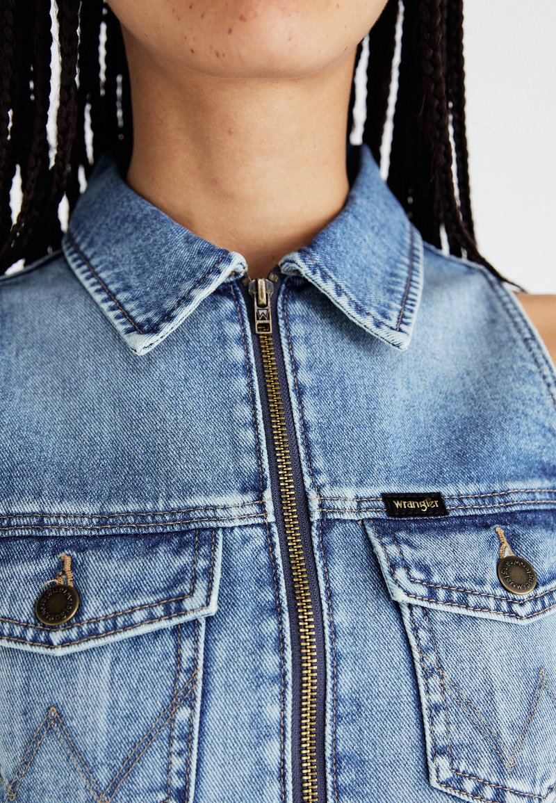 Dunkelblauer Denim-Weste mit Kragen, Frontreißverschluss und zwei Brusttaschen. Ausgestattet mit bronzefarbenen Beschlägen und einem kleinen schwarzen Etikett mit der Aufschrift "Wrangler".