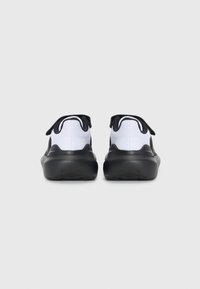 Des chaussures de sport noir et blanc présentent un upper en tissu texturé avec une semelle lisse noire et des accents au talon. Un design minimaliste avec des languettes au talon.
