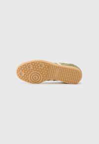 Grøn og hvid sneaker sål med en tekstureret gummibas, der har cirkulære og hexagonale grebmønstre samt et præget brandlogo.