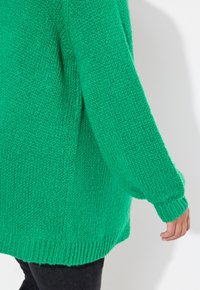 Maglione verde a maglia con vestibilità ampia, di spessore spesso e maniche lunghe. L'orlo e i polsini sono a coste, il che ne esalta lo stile informale.