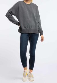 Grijze sweatshirt van zacht materiaal, met een ronde hals en geribde zoom. Gepaard met donkergijze skinny jeans en witte sneakers met multikleurige accenten.