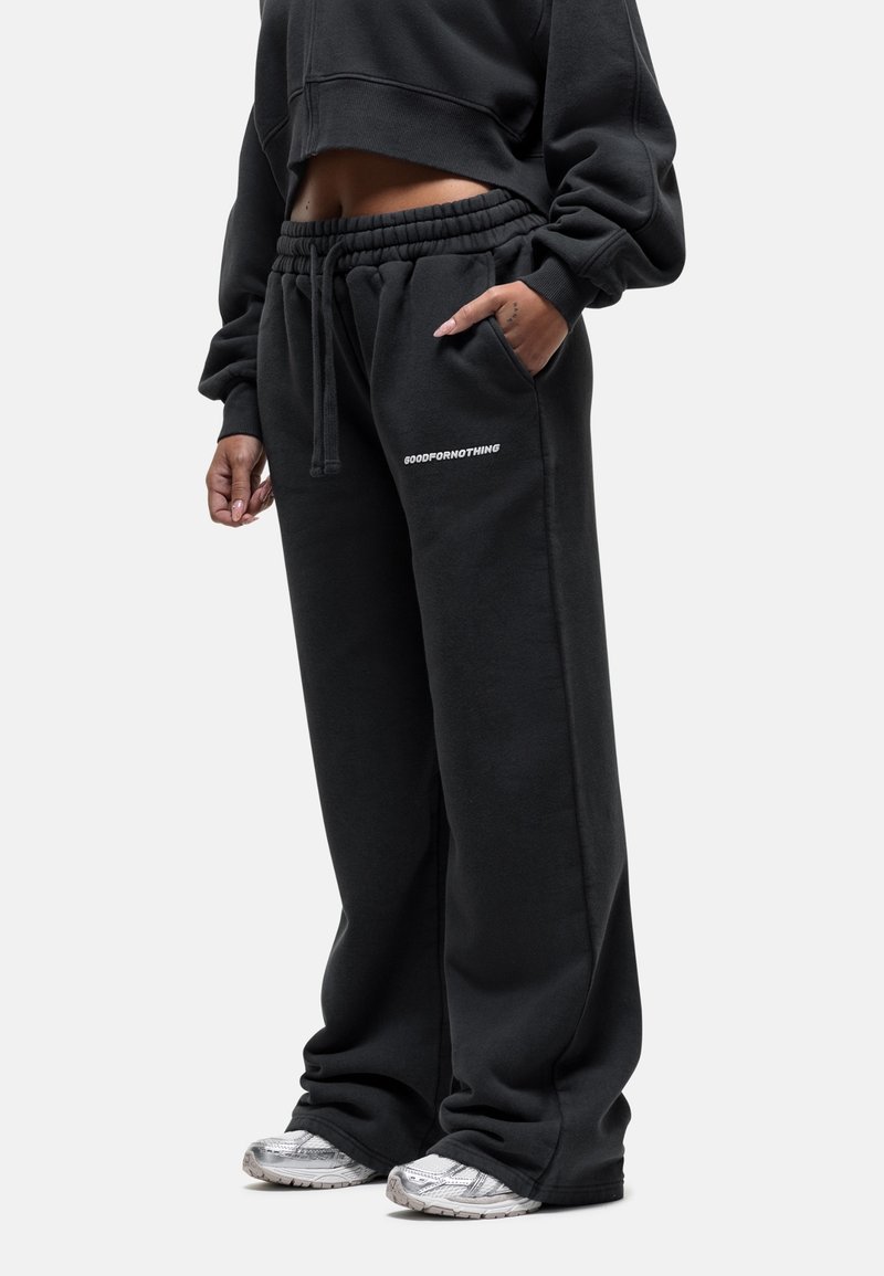 Czarna krótka bluza i luźne czarne spodnie dresowe z elastycznym pasem; na spodniach widnieje biały napis z logo. Srebrne sneakersy.