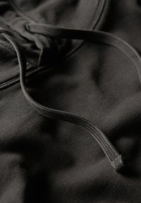Black textile fabric with a smooth texture and a braided drawstring accent. Close-up view highlighting stitching and material details.