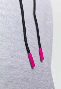 Felpa grigia con corde nere dotate di punte in plastica rosa stampate con la parola "GUESS". Texture liscia e design casual.